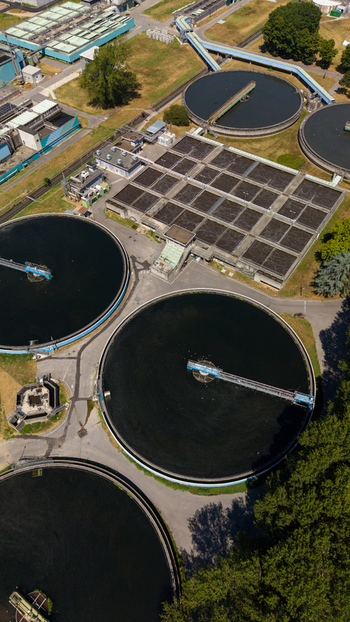 Aerial view of a wastewater treatment plant featuring large circular sedimentation tanks and rectangular aeration basins surrounded by trees in Milan Lombardy Italy. Aerial view of a wastewater treatment plant featuring large circular sedimentation tanks and rectangular aeration basins surrounded by trees in Milan Lombardy Italy.