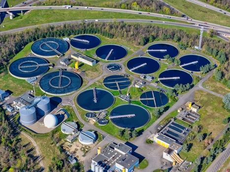 Aerial view of the stark contrast between the dark circular water treatment pools and verdant fields framed by a highway Sausheim Grand Est France.