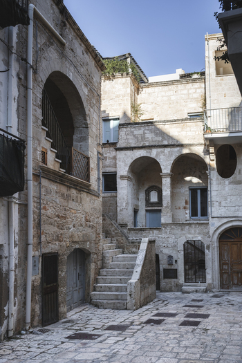 View of historic stone buildings with arched entrances external staircases and balconies under a clear blue sky in the old town of Polignano a Mare Apulia Italy.