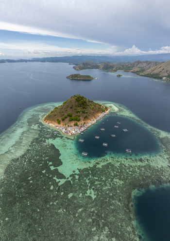 Aerial view of Pulau Kukusan surrounded by turquoise coral reefs clear blue waters and floating fish farms in Komodo East Nusa Tenggara Indonesia. Aerial view of Pulau Kukusan surrounded by turquoise coral reefs clear blue waters and floating fish farms in Komodo East Nusa Tenggara Indonesia.