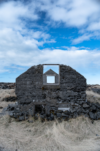 View of abandoned farmhouse ruins with empty window frames and stone walls under a cloudy blue sky Hafnarfjordur Hafnarfjardarkaupstad Iceland. View of abandoned farmhouse ruins with empty window frames and stone walls under a cloudy blue sky Hafnarfjordur Hafnarfjardarkaupstad Iceland.