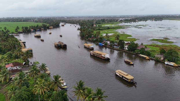Aerial view of traditional houseboats navigating the calm waters of the Alleppey Backwaters surrounded by lush palm trees and greenery in Alappuzha Kerala India. Aerial view of traditional houseboats navigating the calm waters of the Alleppey Backwaters surrounded by lush palm trees and greenery in Alappuzha Kerala India.