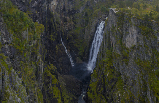 Aerial view of Voringfossen waterfall plunging into a deep rocky canyon surrounded by steep mossy cliffs and lush greenery in Eidfjord Municipality Vestland Norway.