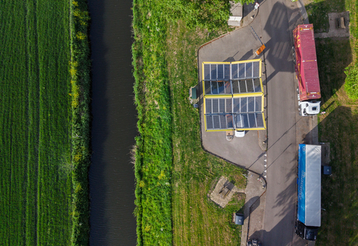 Aerial view of the Fastned Charging Station with solar panel roofs parked trucks and a narrow canal next to green fields in Vierpolders Zuid Holland Netherlands. Aerial view of the Fastned Charging Station with solar panel roofs parked trucks and a narrow canal next to green fields in Vierpolders Zuid Holland Netherlands.