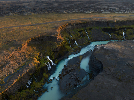 Aerial view of milky blue water carves through a dark rocky canyon where delicate waterfalls cascade into the river below Sigöldugljúfur Rangárþing ytra Iceland. Aerial view of milky blue water carves through a dark rocky canyon where delicate waterfalls cascade into the river below Sigöldugljúfur Rangárþing ytra Iceland.