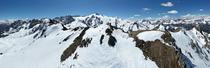Aerial view of Pointe Ronde mountain peak with snow covered ridges rocky outcrops and skiers standing on the summit under a clear blue sky in Trient Valais Switzerland.