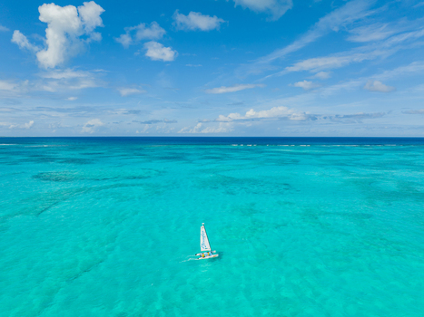 Aerial view of a small catamaran sailing on the clear turquoise waters of Grace Bay under a bright blue sky Grace Bay Caicos Islands Turks and Caicos Islands. Aerial view of a small catamaran sailing on the clear turquoise waters of Grace Bay under a bright blue sky Grace Bay Caicos Islands Turks and Caicos Islands.