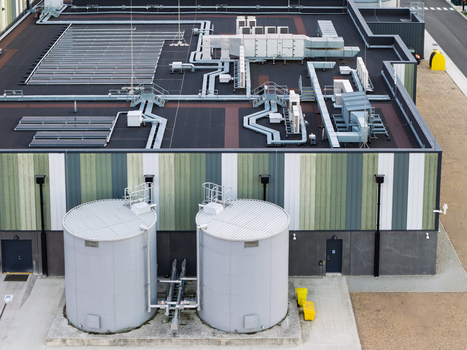 Aerial view of a data center facility featuring large cylindrical water tanks and industrial HVAC equipment on the roof in the United Kingdom. Aerial view of a data center facility featuring large cylindrical water tanks and industrial HVAC equipment on the roof in the United Kingdom.