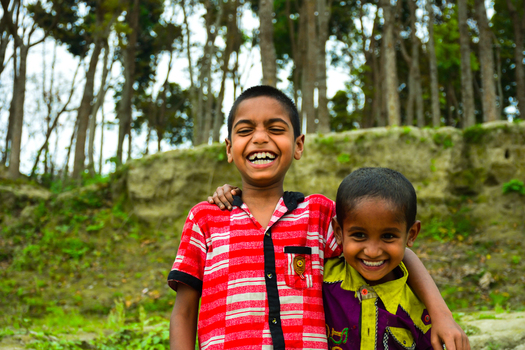 Kushtia Bangladesh 12 March 2020 View of two young boys smiling and embracing each other in front of a wooded area with tall trees and an earthen bank. Kushtia Bangladesh 12 March 2020 View of two young boys smiling and embracing each other in front of a wooded area with tall trees and an earthen bank.