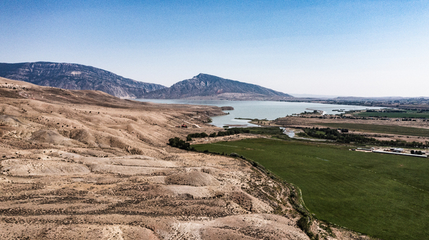 Aerial view of the landscape near Cody featuring a large lake arid rolling hills and vibrant green agricultural fields in Cody Wyoming United States.