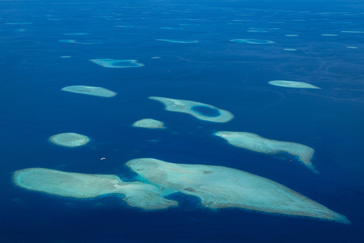 Aerial view of coral atolls and turquoise lagoons scattered across the deep blue Indian Ocean Maldives.