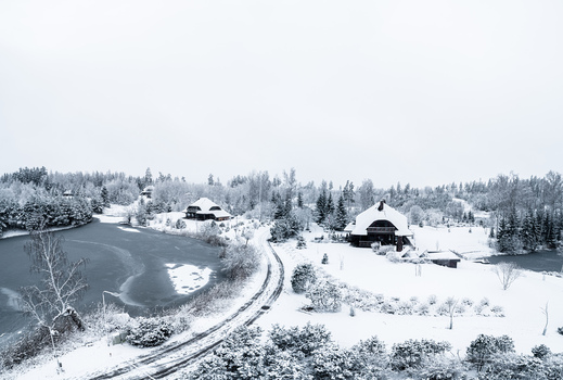 Aerial view of a snow covered landscape in Latvia featuring a frozen lake wooden houses a winding road and snow laden trees under a winter sky Latvia. Aerial view of a snow covered landscape in Latvia featuring a frozen lake wooden houses a winding road and snow laden trees under a winter sky Latvia.