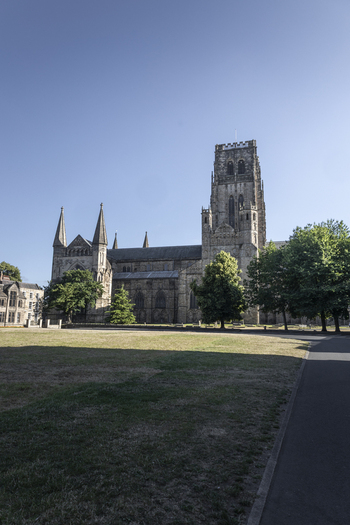 View of the historic Durham Cathedral with its prominent central tower surrounded by lush green trees and a clear blue sky in Durham England United Kingdom. View of the historic Durham Cathedral with its prominent central tower surrounded by lush green trees and a clear blue sky in Durham England United Kingdom.