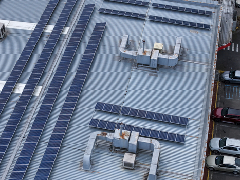 Melbourne Australia 25 September 2026 Aerial view of a warehouse roof featuring rows of solar panels industrial ventilation units and a parking lot with cars below.