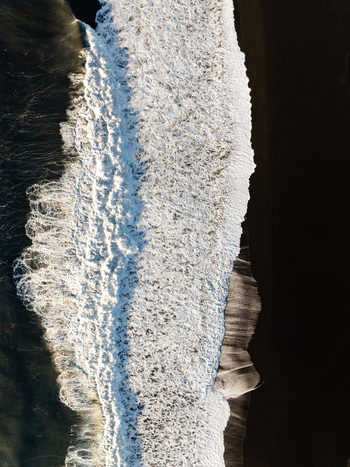 Aerial view of white sea foam crashing onto the dark volcanic black sand beach in Reykjanesbaer Iceland. Aerial view of white sea foam crashing onto the dark volcanic black sand beach in Reykjanesbaer Iceland.