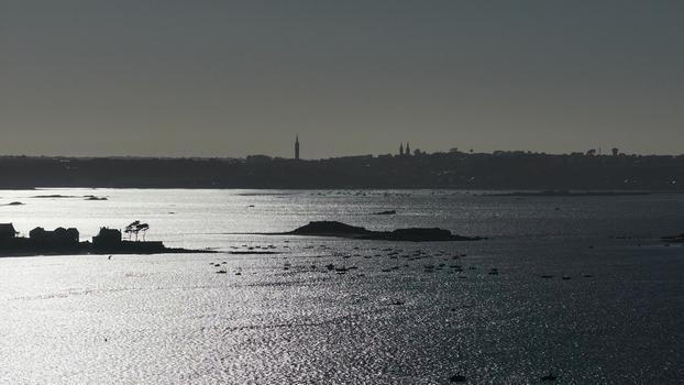 Aerial view of shimmering waters reflect the distant silhouette of the city against the pale sky creating a serene yet striking contrast Carantec Finistre France.