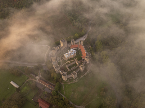 Aerial view of Manasija Monastery surrounded by morning fog featuring historic stone fortifications towers and a church dome amidst green fields in Despotovac Pomoravski okrug Serbia.