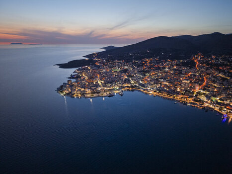 Aerial view of the coastal city of Saranda at twilight with illuminated buildings harbor lights and the Ionian Sea coastline in Saranda Vlore County Albania. Aerial view of the coastal city of Saranda at twilight with illuminated buildings harbor lights and the Ionian Sea coastline in Saranda Vlore County Albania.