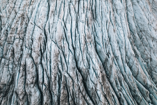 Aerial view of the textured surface of Skaftafell glacier featuring deep blue crevasses and dark volcanic ash streaks in Skaftafell Sveitarfelagid Hornaf Iceland. Aerial view of the textured surface of Skaftafell glacier featuring deep blue crevasses and dark volcanic ash streaks in Skaftafell Sveitarfelagid Hornaf Iceland.