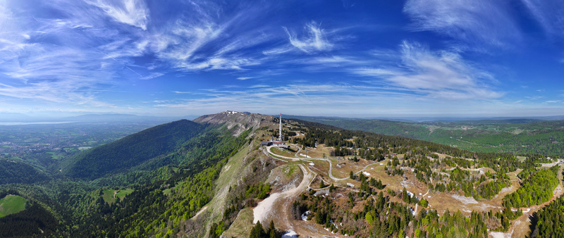 Aerial view of Col de la Faucille mountain pass with its telecommunications tower winding roads and lush green slopes under a bright blue sky Gex Auvergne Rhone Alpes France. Aerial view of Col de la Faucille mountain pass with its telecommunications tower winding roads and lush green slopes under a bright blue sky Gex Auvergne Rhone Alpes France.
