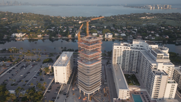 Aerial view of a high rise building under construction with a tall crane surrounded by residential buildings a canal and lush greenery in Miami Beach Florida United States. Aerial view of a high rise building under construction with a tall crane surrounded by residential buildings a canal and lush greenery in Miami Beach Florida United States.