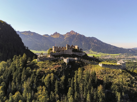 Aerial view of Burg Hohenwerfen perched on a rocky hill surrounded by dense pine forests with the majestic Alps in the background under a clear blue sky in Werfen Salzburg Austria. Aerial view of Burg Hohenwerfen perched on a rocky hill surrounded by dense pine forests with the majestic Alps in the background under a clear blue sky in Werfen Salzburg Austria.