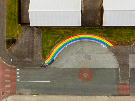 Aerial view of a vibrant rainbow painted curb bordering a paved area next to a building with white roofs and road markings in Iceland. Aerial view of a vibrant rainbow painted curb bordering a paved area next to a building with white roofs and road markings in Iceland.