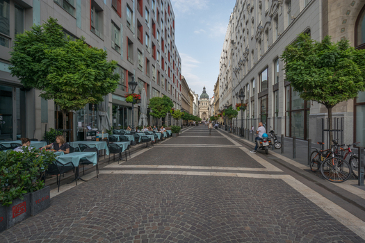 View of St. Stephen s Basilica at the end of a pedestrian street lined with outdoor cafe tables trees and modern buildings in Budapest Hungary.