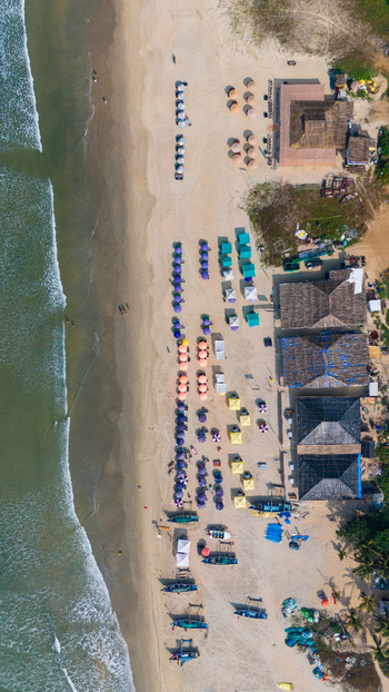 Aerial view of Benaulim Beach featuring colorful umbrellas beach shacks and gentle waves on the sandy shore in South Goa Goa India.