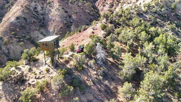 Collbran Colorado United States 04 July 2026 Aerial view of a hunting observation tower on a ridge with a red UTV parked nearby surrounded by trees and rocky terrain.