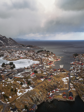 Aerial view of the village nestled between the jagged coastline and the icy waters a tapestry of red roofs against the snow dusted landscape Tind Nordland Norway.