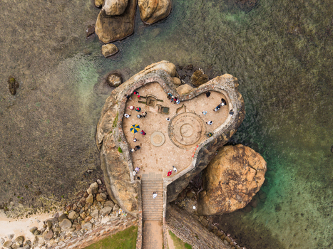 Aerial view of a heart shaped stone platform with people standing on it surrounded by clear ocean water and rocky formations in Galle Southern Province Sri Lanka. Aerial view of a heart shaped stone platform with people standing on it surrounded by clear ocean water and rocky formations in Galle Southern Province Sri Lanka.