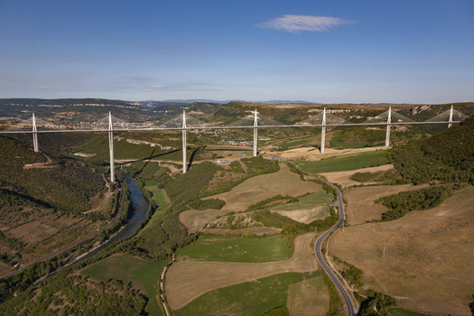 Aerial view of the Millau Viaduct piercing the sky above the lush green valley a modern marvel against the backdrop of rolling hills Millau France. Aerial view of the Millau Viaduct piercing the sky above the lush green valley a modern marvel against the backdrop of rolling hills Millau France.