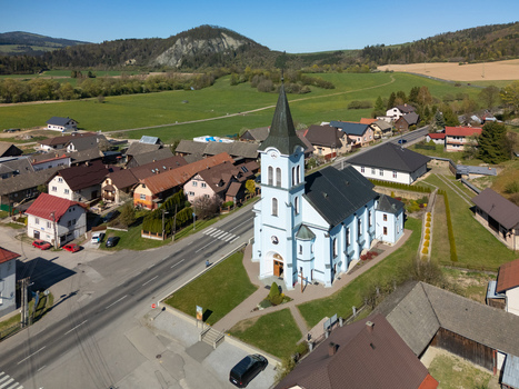Aerial view of the light blue Church of St. Joseph surrounded by village houses and green hills under a clear sky in Kriva Zilina Region Slovakia.