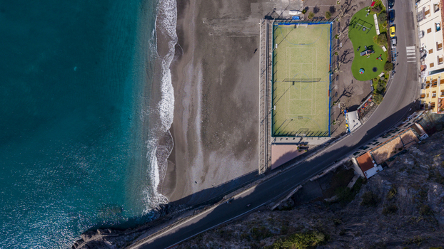 Aerial view of the dark sandy beach meeting the turquoise ocean next to a tennis court and colorful buildings Minori Salerno Italy Aerial view of the dark sandy beach meeting the turquoise ocean next to a tennis court and colorful buildings Minori Salerno Italy