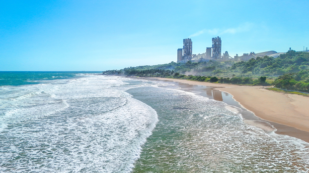 Aerial view of a cement factory situated on a lush hill overlooking a sandy beach and the ocean in Indonesia.