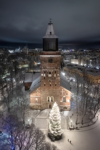 Aerial view of Turku Cathedral illuminated at night with a large glowing Christmas tree in the snow covered square surrounded by the city skyline in Turku Varsinais Suomi Finland. Aerial view of Turku Cathedral illuminated at night with a large glowing Christmas tree in the snow covered square surrounded by the city skyline in Turku Varsinais Suomi Finland.