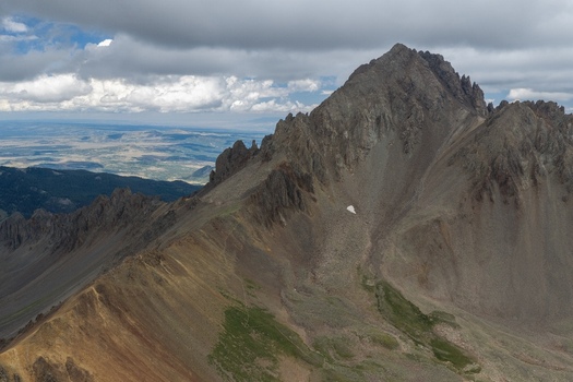 Aerial view of Mount Sneffels in the San Juan Mountains with rugged rocky peaks steep slopes and patches of green vegetation in Ouray County Colorado United States. Aerial view of Mount Sneffels in the San Juan Mountains with rugged rocky peaks steep slopes and patches of green vegetation in Ouray County Colorado United States.