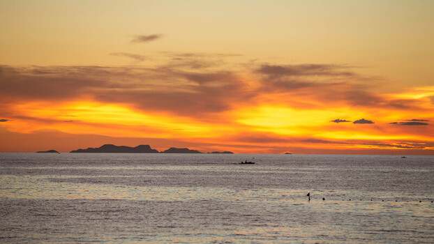 View of Bantayan Island silhouetted against a vibrant golden sunset over the sea with a small boat crossing the horizon in Cebu Central Visayas Philippines. View of Bantayan Island silhouetted against a vibrant golden sunset over the sea with a small boat crossing the horizon in Cebu Central Visayas Philippines.