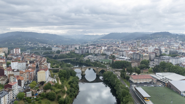 Ourense Spain 30 April 2026 Aerial view of Ponte Vella de Ourense spanning the Minho River with the city skyline historic buildings and lush green riverbanks under an overcast sky.