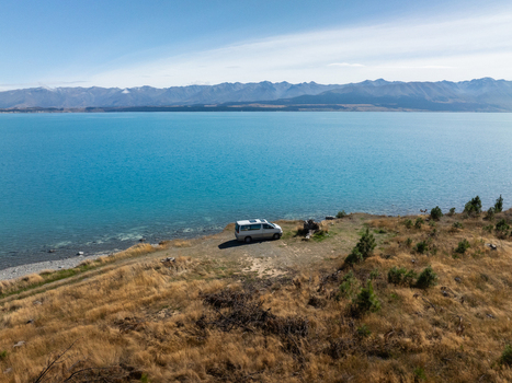 Aerial view of a lone van sits poised on the edge of golden grasslands overlooking the vast expanse of Lake Tekapo s turquoise waters Lake Tekapo Otago Region New Zealand. Aerial view of a lone van sits poised on the edge of golden grasslands overlooking the vast expanse of Lake Tekapo s turquoise waters Lake Tekapo Otago Region New Zealand.