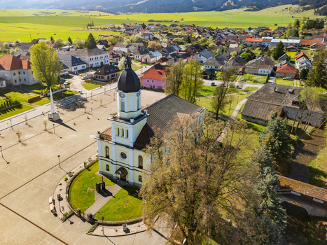 Aerial view of the Evangelical church and main square surrounded by traditional houses and green rolling hills in Partizanska Lupca Zilina Region Slovakia.
