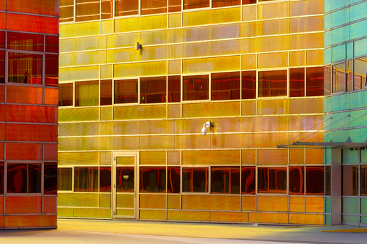 View of modern buildings with orange yellow and green glass panels casting vibrant reflections under the sun La Defense Flevoland Netherlands. View of modern buildings with orange yellow and green glass panels casting vibrant reflections under the sun La Defense Flevoland Netherlands.