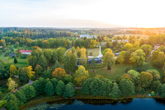 Aerial view of a lush forest landscape with a lake in the foreground scattered buildings and golden hour sunlight in Latvia. Aerial view of a lush forest landscape with a lake in the foreground scattered buildings and golden hour sunlight in Latvia.