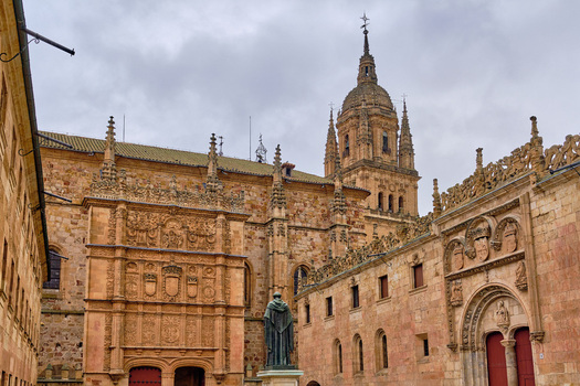 Salamanca Spain 29 November 2025 View of the ornate Plateresque facade of the University of Salamanca with the statue of Fray Luis de Leon and the cathedral tower under a cloudy sky.
