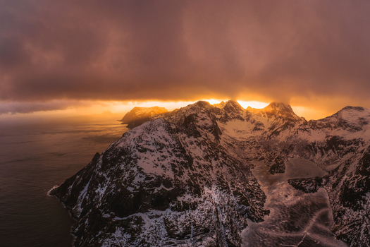 Aerial view of snow dusted peaks pierce through the golden light casting long shadows over the fjords and icy waters Lofoten Nordland Norway.