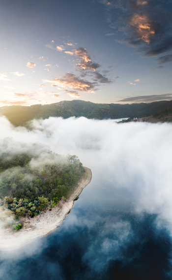 Aerial view of Kangaroo Creek Reservoir with thick white fog rolling over the water and forested hills under a sunset sky Adelaide Hills Council South Australia Australia. Aerial view of Kangaroo Creek Reservoir with thick white fog rolling over the water and forested hills under a sunset sky Adelaide Hills Council South Australia Australia.