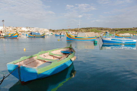 View of vibrant blue and yellow boats floating peacefully on the serene water reflecting the clear sky in Marsaxlokk Malta. View of vibrant blue and yellow boats floating peacefully on the serene water reflecting the clear sky in Marsaxlokk Malta.