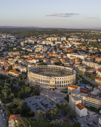 Aerial view of Pula Arena surrounded by historic stone architecture orange rooftops and lush greenery in the coastal city of Pula Istarska zupanija Croatia. Aerial view of Pula Arena surrounded by historic stone architecture orange rooftops and lush greenery in the coastal city of Pula Istarska zupanija Croatia.
