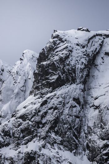 View of snow covered jagged mountain peaks and rocky cliffs under a clear sky in Kvaloya Troms Norway. View of snow covered jagged mountain peaks and rocky cliffs under a clear sky in Kvaloya Troms Norway.